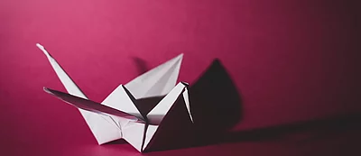 Weißer Origami-Kranich vor pinkem Hintergrund